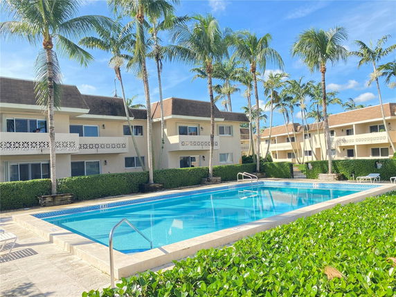 Outdoor swimming pool area with surrounding residential buildings and palm trees.