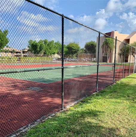 Tennis court enclosed with a chain-link fence, adjacent to a building.