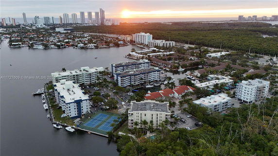 Aerial view of residential buildings near a waterfront with skyscrapers in the distance during sunset.