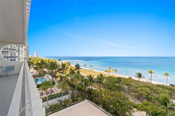 Balcony view overlooking a beach and ocean with palm trees and nearby buildings.