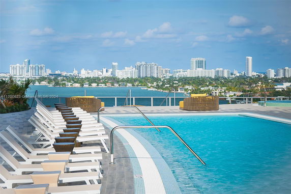 Rooftop area with a swimming pool and lounge chairs, offering views of a city skyline across the water.