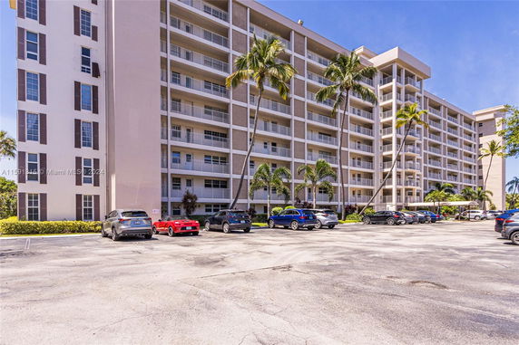 View of an apartment building with a surface parking area in front.