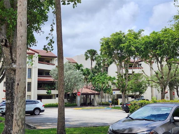 Front view of a multi-story residential building surrounded by trees and a parking area.