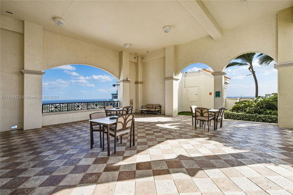 Outdoor area on a rooftop with tables and chairs, featuring arched openings and views of the ocean.