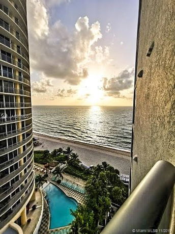 Panoramic view from a high-rise building overlooking a pool, beach, and ocean during sunset.