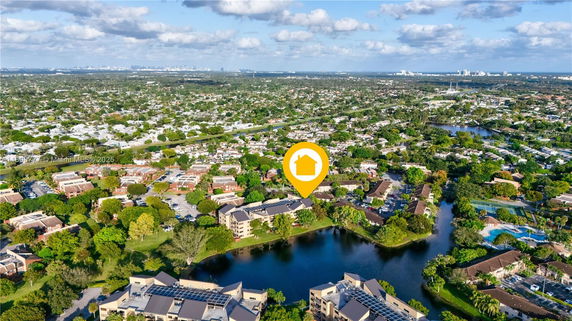 Aerial panoramic view of a residential area with multiple buildings, surrounded by greenery and water bodies.