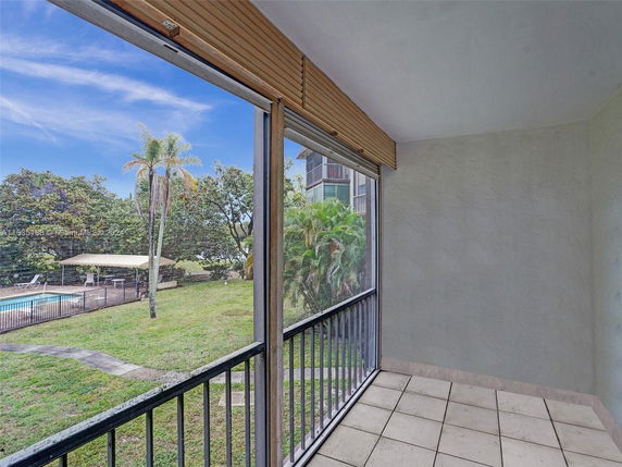View through a balcony of a landscaped area with a swimming pool and palm trees.
