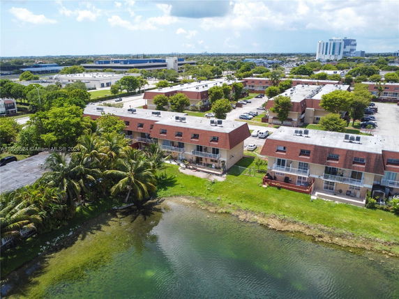 Aerial view of townhouses by a body of water with parking areas and other buildings visible in the background.