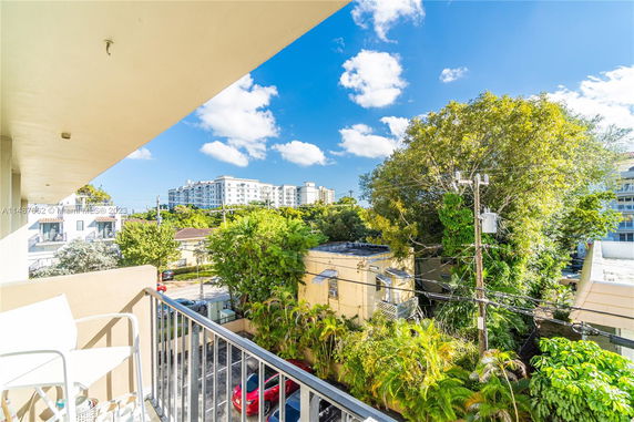 View from a balcony showing nearby buildings, trees, and a clear sky.