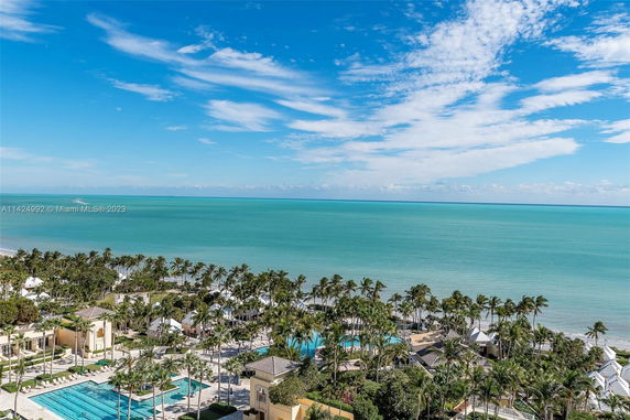 Panoramic view of a coastal area with buildings and swimming pools surrounded by palm trees, overlooking the ocean.