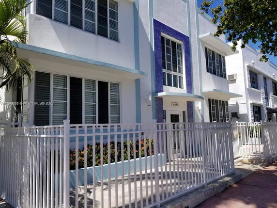 Front view of a two-story building with a white and blue facade and fenced entrance.
