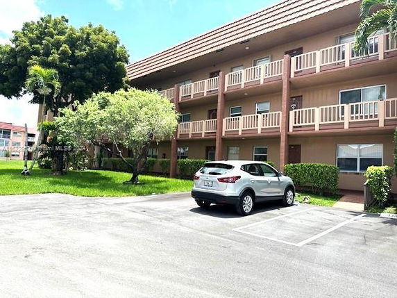 Outdoor parking area in front of a three-story building with balconies.