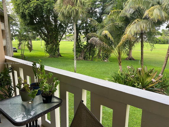View from a balcony showing a grassy area with trees and plants.
