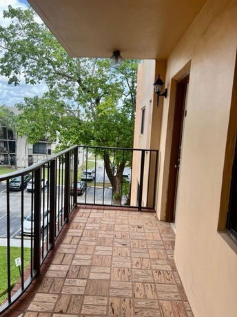 View from a balcony with railing, showing parking area and trees.