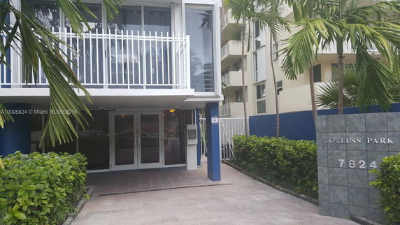 Front view of a modern multi-story building with a prominent entrance and glass balconies.