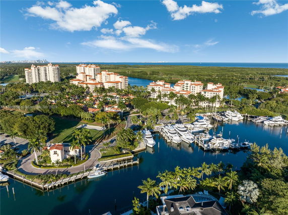 Aerial panoramic view of residential buildings near a marina with yachts and lush greenery in the background.