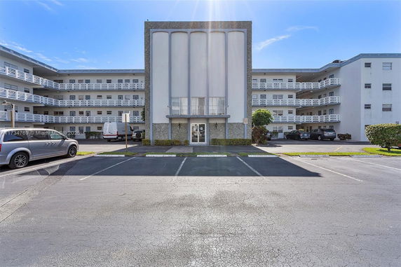 Front view of a multi-story residential building with balconies and parking spaces.