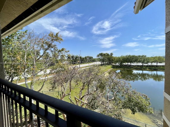 View from a balcony showing trees, a pond, and a road with palm trees in the background.