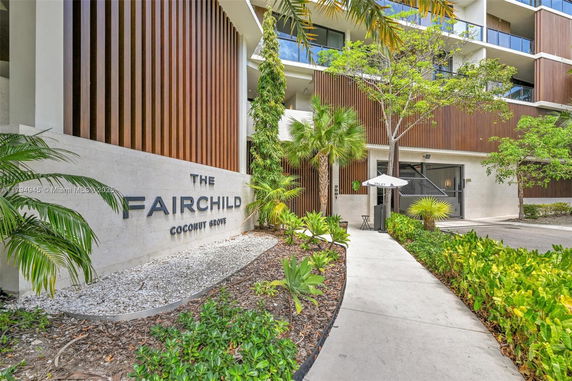 Front view of a modern multi-story building with wooden accents and landscaped entrance.