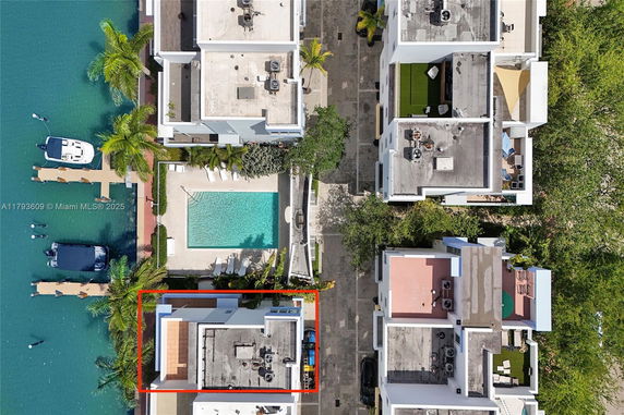 Aerial view of buildings with flat rooftops, some featuring air conditioning units and seating areas, alongside a swimming pool and docking area.