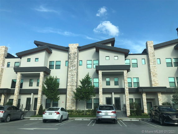 Front view of a modern multi-story residential building with stone accents and parking space.