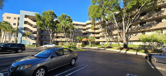 Front view of a multi-story residential building with balconies and surrounding trees.