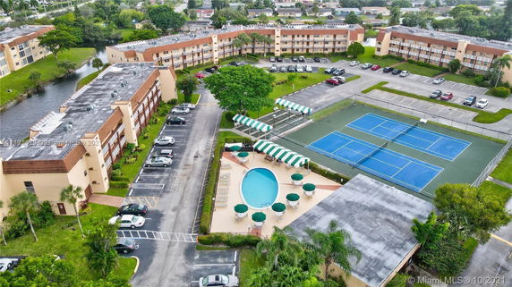 Aerial view of a residential complex with tennis courts, swimming pool, and parking area.