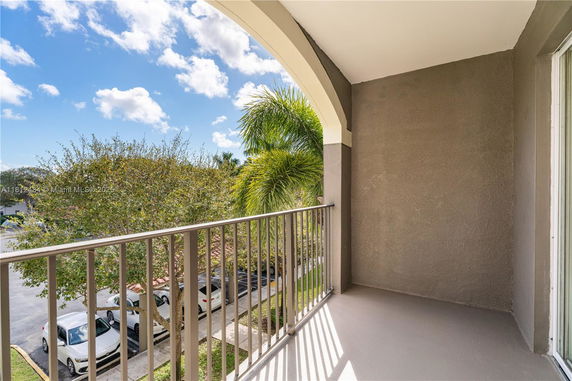View from a balcony overlooking trees and parked cars, with a clear sky in the background.