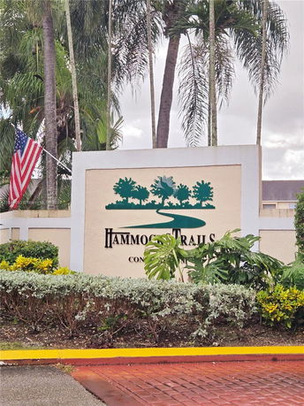 Entrance sign for Hammocks Trails with greenery and American flag.
