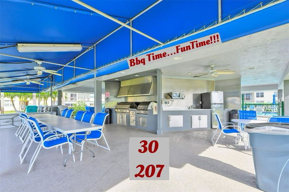 Outdoor area with BBQ facilities, tables, and chairs under a blue canopy.
