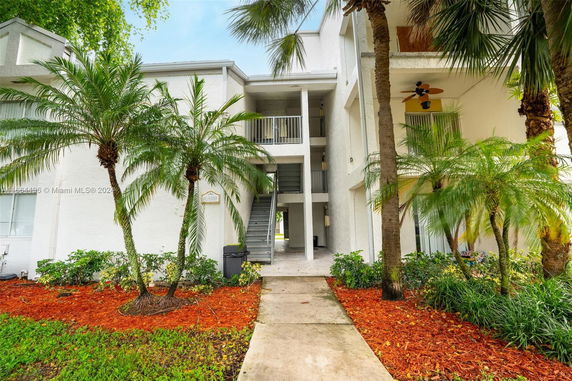 Front view of a multi-story building with exterior stairs and balconies surrounded by palm trees.