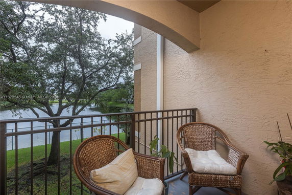 Balcony with wicker chairs overlooking a lake and trees.