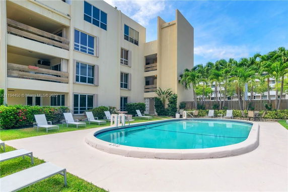 Outdoor swimming pool in front of a multi-story residential building with balconies.
