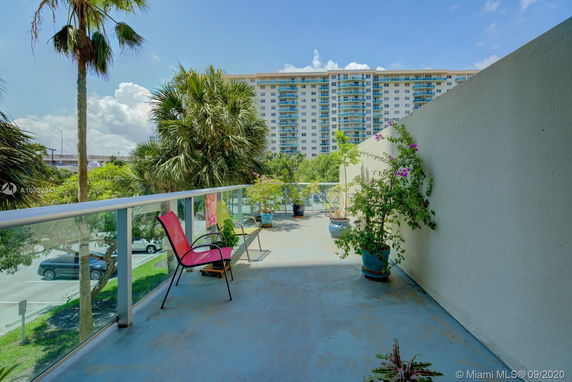 Rooftop patio with seating and plants, overlooking a tall apartment building.