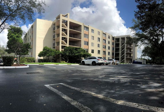 Front view of a multi-story apartment building with balconies and parking area.