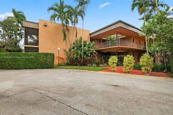 Front view of a two-story building with a balcony and tropical landscaping.