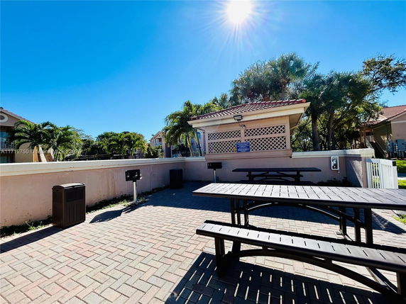 Outdoor area with picnic tables and nearby buildings under a clear blue sky.