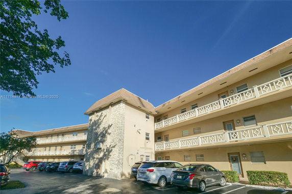 Front view of a three-story building with balconies and parking area.