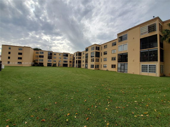 Front view of a multi-story apartment building with yellowish-brown exterior and large windows.