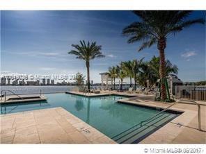 View of a swimming pool area overlooking a waterfront with cityscape in the distance.