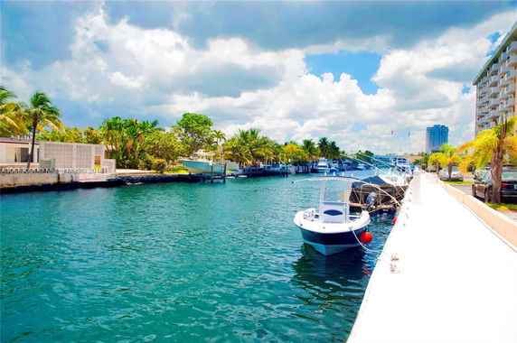 View of a canal with boats docked alongside a waterfront area and buildings in the distance.