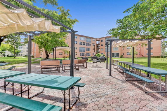 Outdoor area with picnic tables and benches under pergolas near an apartment complex.