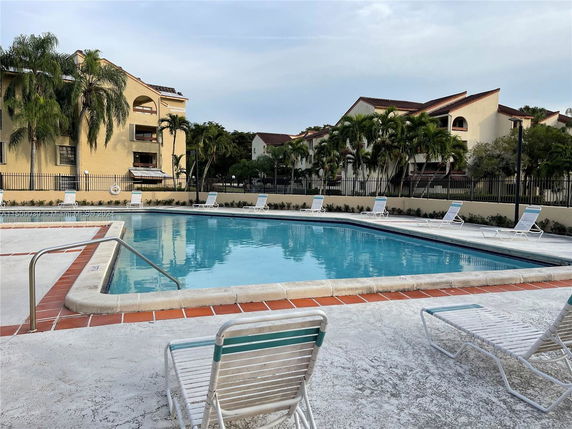 Outdoor swimming pool with lounge chairs surrounding it, adjacent to residential buildings.