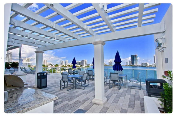 Outdoor patio area with tables and umbrellas overlooking water and city skyline.