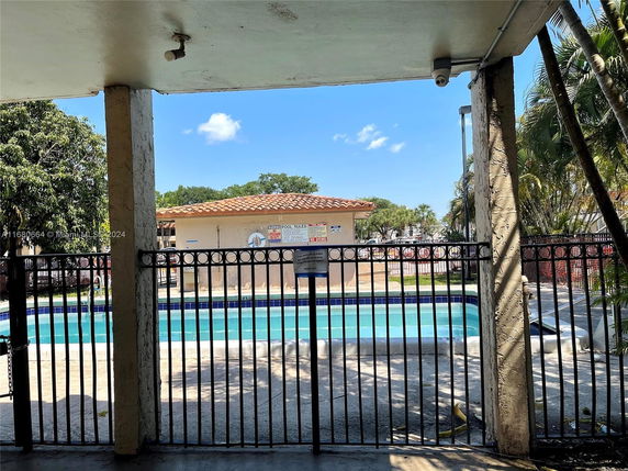 View of a swimming pool area with a fence and a small building in the background.