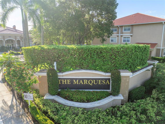 Front view of a residential building with a sign reading 'The Marquesa' surrounded by greenery.