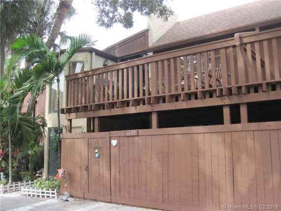 Front view of a two-story wooden house with a balcony and gated entrance.