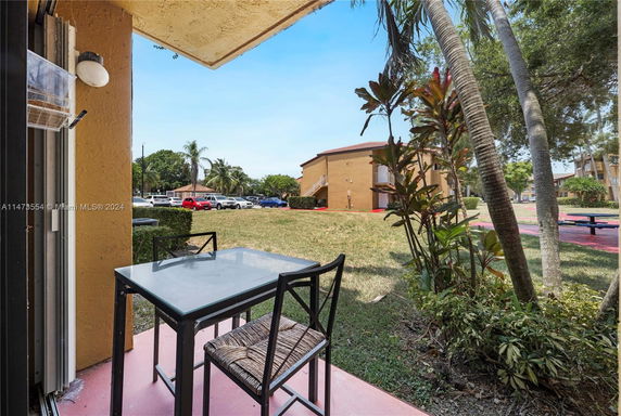 View from a patio showing a grassy area, plants, and parked cars in front of a brown building.