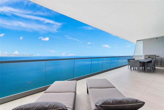 Wide angle view of the ocean from a building balcony with seating area.