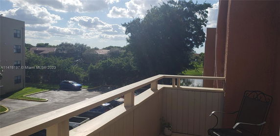 View from a balcony overlooking trees, parked cars, and distant buildings.